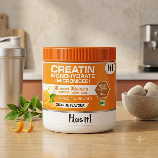 A tub of creatin monohydrate powder in orange flavor sits on a wooden countertop in a kitchen setting. The container is white with a bright orange lid and orange label accents.
