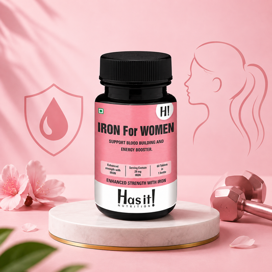 A bottle of Hasit! Nutrition 'Iron For Women' dietary supplement centered on a white marble pedestal. The background is a soft pink with decorative elements including a silhouette of a woman, a dumbbell, pink flowers, and a shield icon with a blood drop.